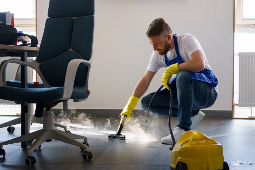 Cleaner steam cleaning an office floor beside a desk chair